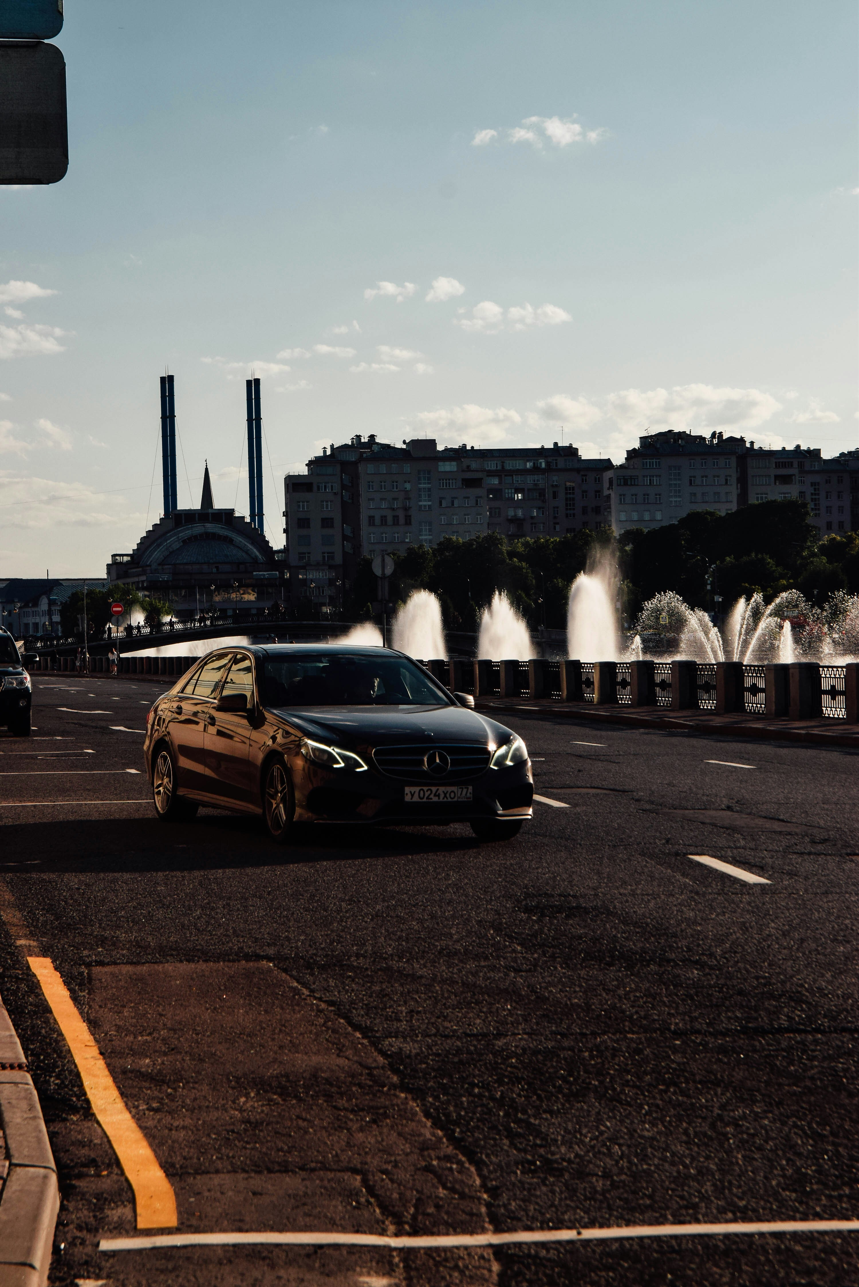 a black car driving down a street next to a fountain