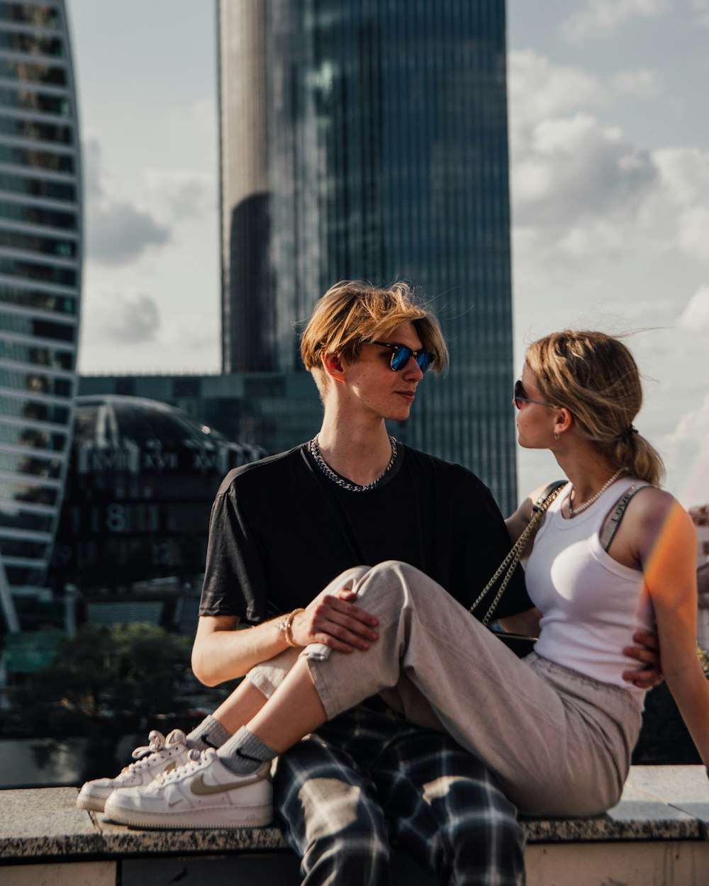 a man and a woman sitting on a ledge in front of a cityscape