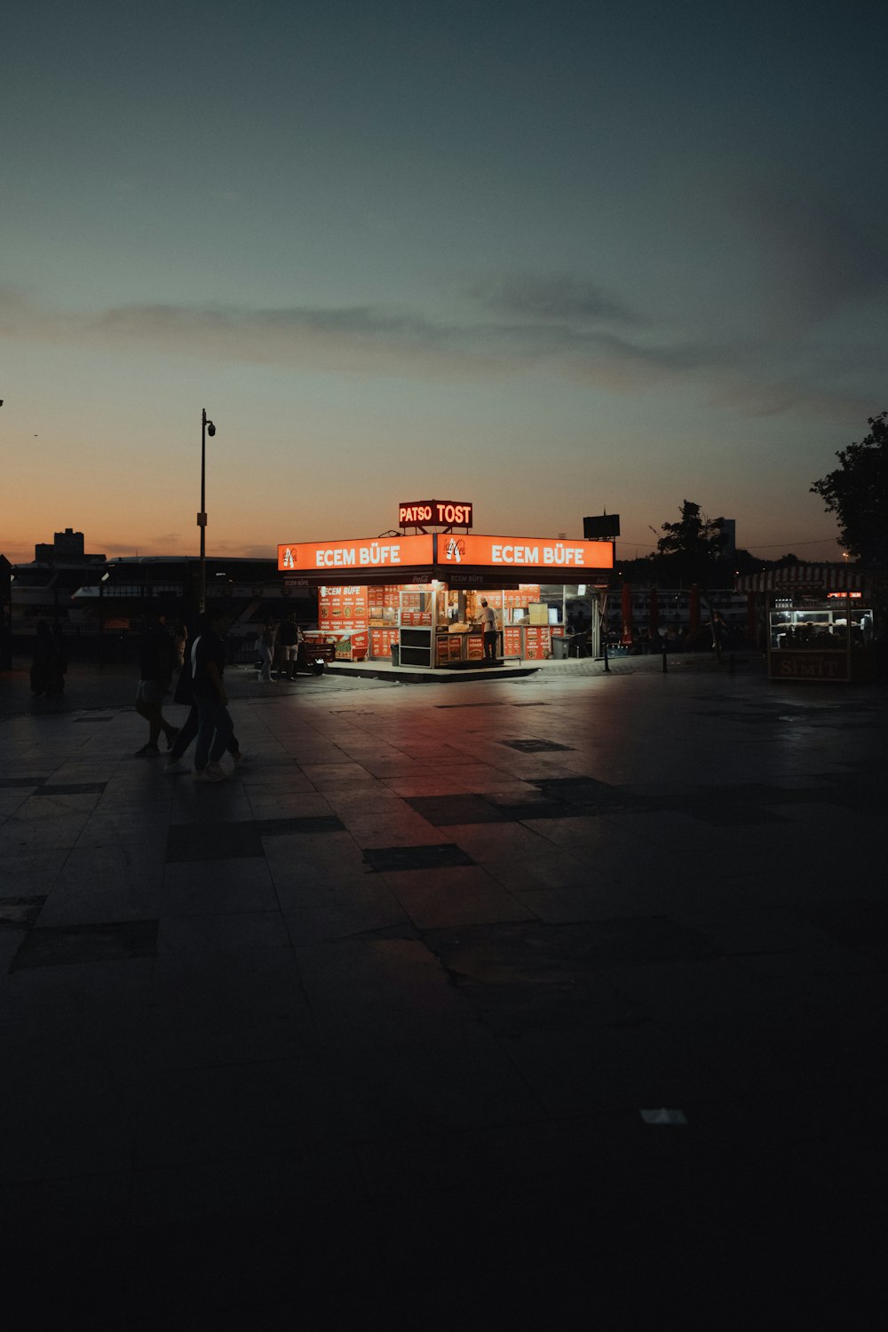 a lit up gas station at night with people walking by