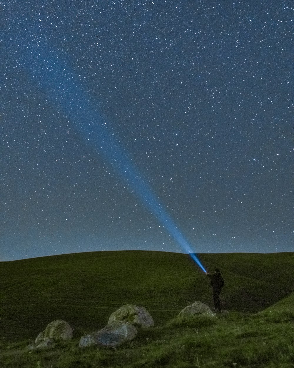 a man standing on top of a lush green hillside under a sky filled with stars