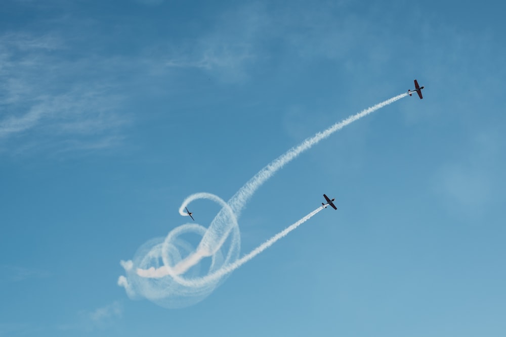 two airplanes flying in the sky leaving a trail of smoke behind them