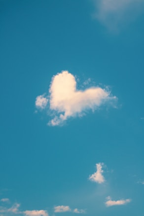 A cloud in the shape of a heart against a clear blue sky, with a few smaller clouds scattered around.