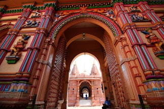 Intricately carved and brightly colored architectural structures are visible, featuring ornate arches and detailed statues that depict figures in traditional attire. The structures are adorned with decorative patterns and vibrant paintwork, emphasizing cultural and historical richness.