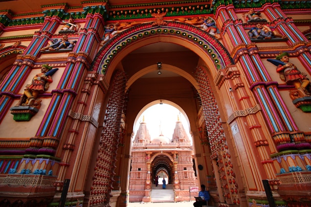 Intricately carved and brightly colored architectural structures are visible, featuring ornate arches and detailed statues that depict figures in traditional attire. The structures are adorned with decorative patterns and vibrant paintwork, emphasizing cultural and historical richness.