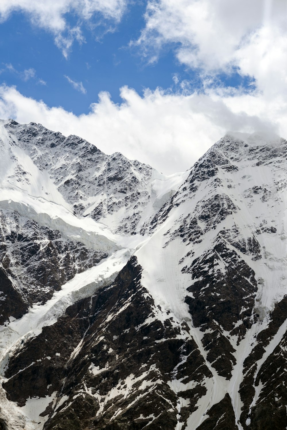 a snow covered mountain range under a cloudy blue sky