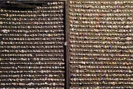 An array of decorative rings is organized in neat horizontal rows against a dark fabric background. Each ring features a variety of gemstones and intricate designs, showcasing a colorful and diverse assortment.