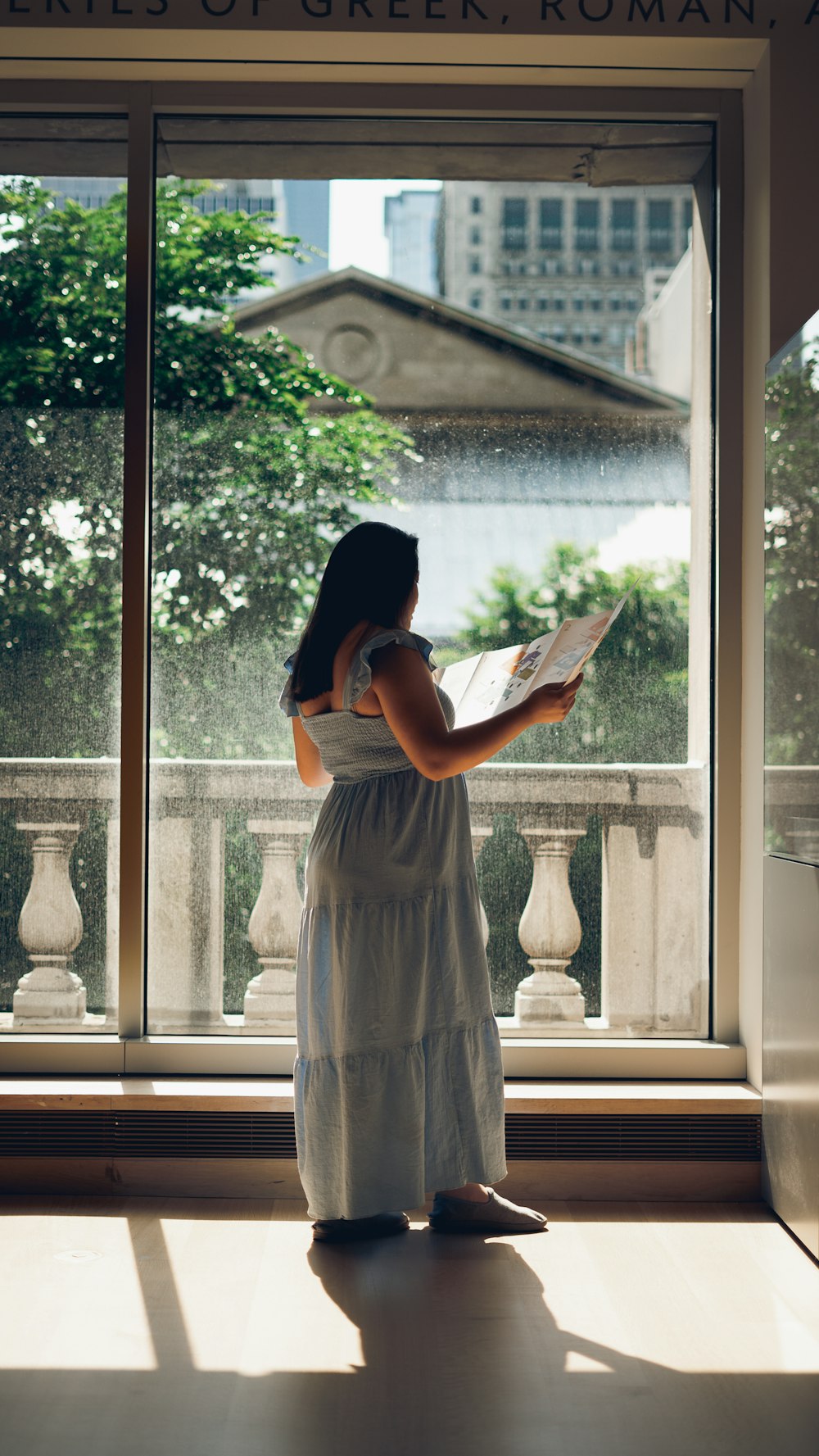 Une femme debout devant une fenêtre en train de lire un livre