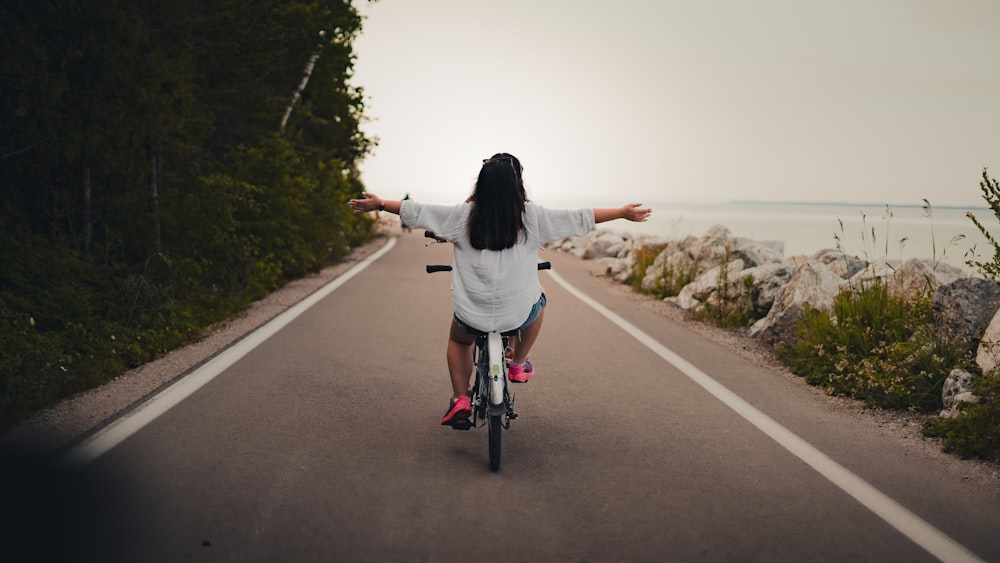 a woman riding a bike down a road next to the ocean