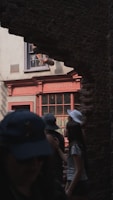 Several people are walking through an archway revealing a shop with a sign reading 'Quality Quidditch'. The scene is partially shaded, with some people wearing hats and casual clothing.