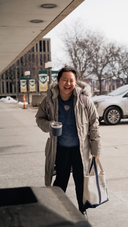 A smiling person holding a reusable shopping bag filled with deanama llc products outdoors.