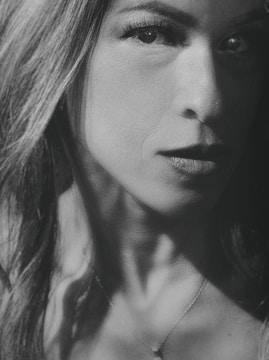 A close-up, black and white portrait emphasizing the person's face, particularly focusing on the eyes and lips. The image captures dramatic lighting and shadows, adding depth and texture to the facial features.