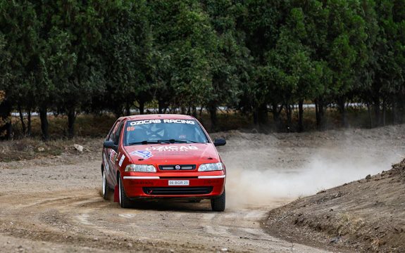 A dynamic shot of the Cambodia Rally Team's car kicking up dust on a rugged dirt track.