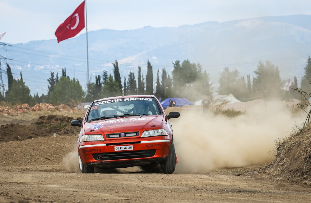 a red car driving down a dirt road