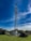 A tall communication tower surrounded by greenery under a vibrant blue sky with scattered clouds. The fenced area at the base contains technical equipment.