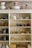 A wooden shelving unit filled with various vintage and ornate items including teapots, pitchers, cups, and decorative glassware. The shelves also display some metal teapots and woven baskets. There are delicate floral and gold patterns on some of the ceramics, adding an antique and elegant touch.