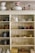 A wooden shelving unit filled with various vintage and ornate items including teapots, pitchers, cups, and decorative glassware. The shelves also display some metal teapots and woven baskets. There are delicate floral and gold patterns on some of the ceramics, adding an antique and elegant touch.