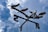 A weather vane features four bird silhouettes perched on a branch, set against a backdrop of partly cloudy blue sky. The cardinal direction letters N, E, S, and W are clearly visible.