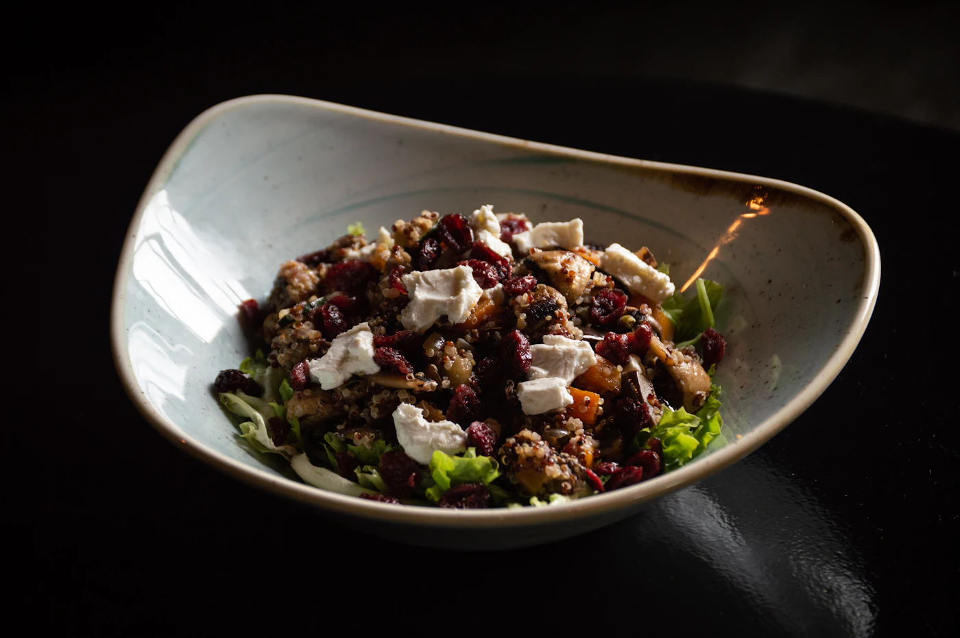 Warm quinoa salad with butternut squash, browned mushrooms, dried cranberries, feta chunks, and tender green leaves