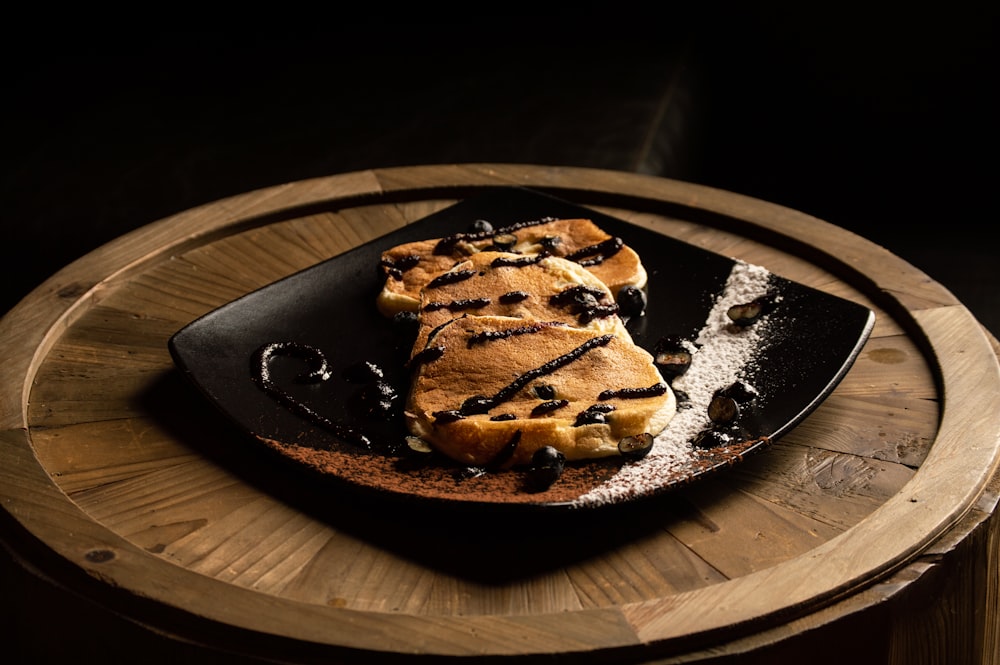 a black plate topped with waffles on top of a wooden table