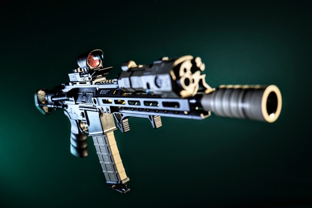 A detailed image of a modern assault rifle with visible attachments, including a scope and a tactical grip. The rifle is positioned at an angle against a dark green background, highlighting its metallic and precision-engineered parts.