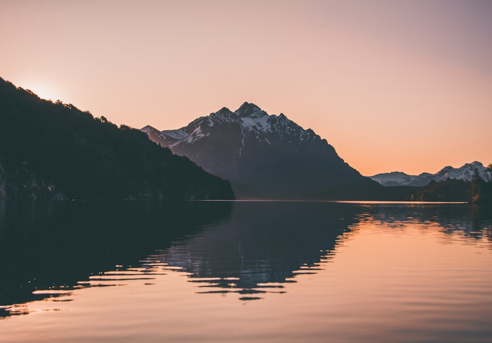 a lake with mountains in the background at sunset