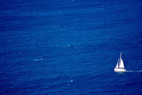 A solitary sailboat with white sails is navigating through a vast expanse of deep blue ocean waters, creating a scene of tranquility and open space.