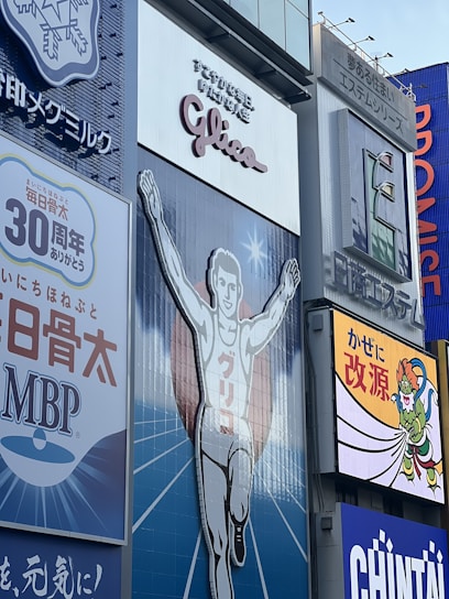 A large advertisement of a runner with arms raised, wearing a white outfit. The backdrop includes additional signage in various colors and languages. The atmosphere is illustrative and commercial with visibility of surrounding billboards.
