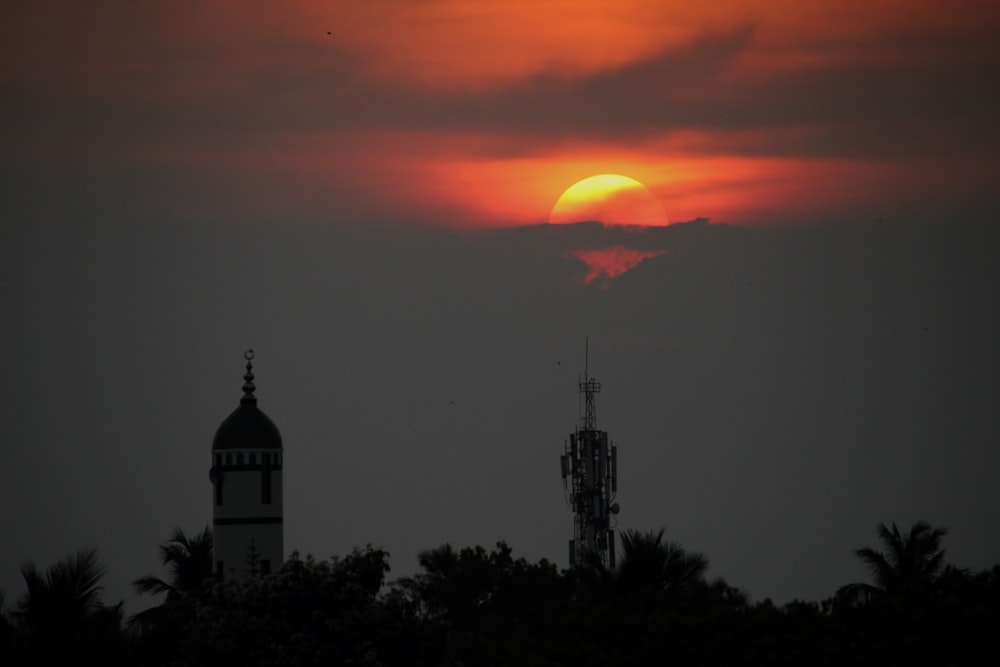 the sun is setting behind a tower with a clock