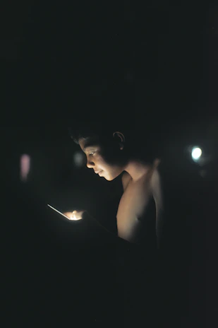 A passionate football fan watching a match on a mobile device, illuminated by the glow of the screen in a dark room.