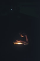 A person is intently reading a book in the dark, illuminated by a warm light source coming from the book itself, creating a focused and intimate atmosphere.