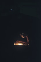A person is intently reading a book in the dark, illuminated by a warm light source coming from the book itself, creating a focused and intimate atmosphere.