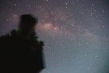 Silhouette of a figure standing under a swirling, starry night sky.