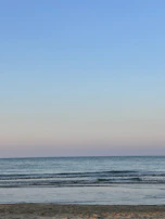 A wide-angle shot of a serene beach with gentle waves under a pastel-colored sky.