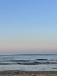 A wide-angle shot of a serene beach with gentle waves under a pastel-colored sky.