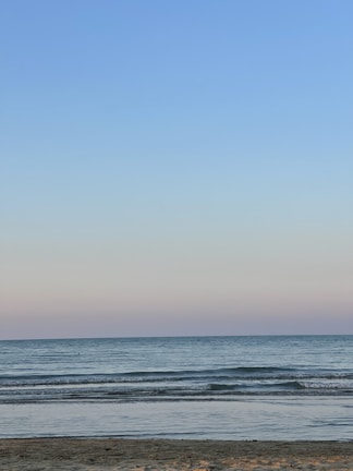 A serene coastal scene with waves gently rolling onto the shore under a vast, pastel sky.