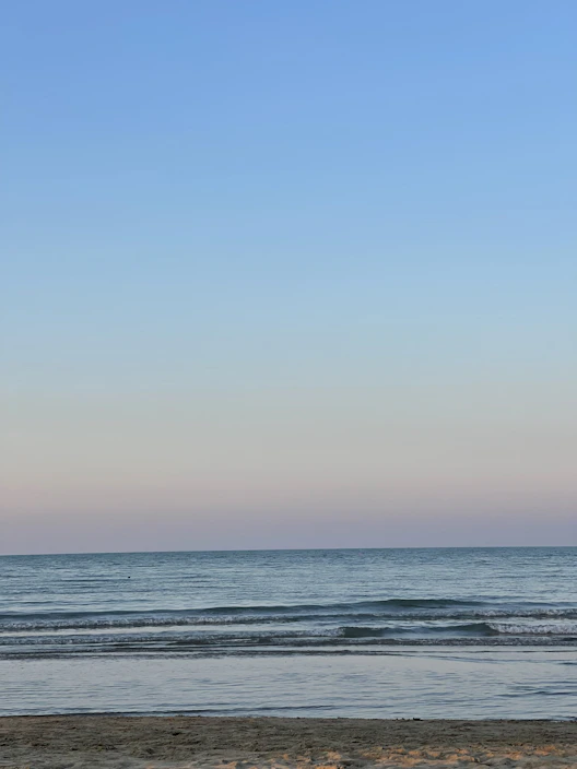 A serene beach scene with soft pastel skies and gentle waves lapping the shore.