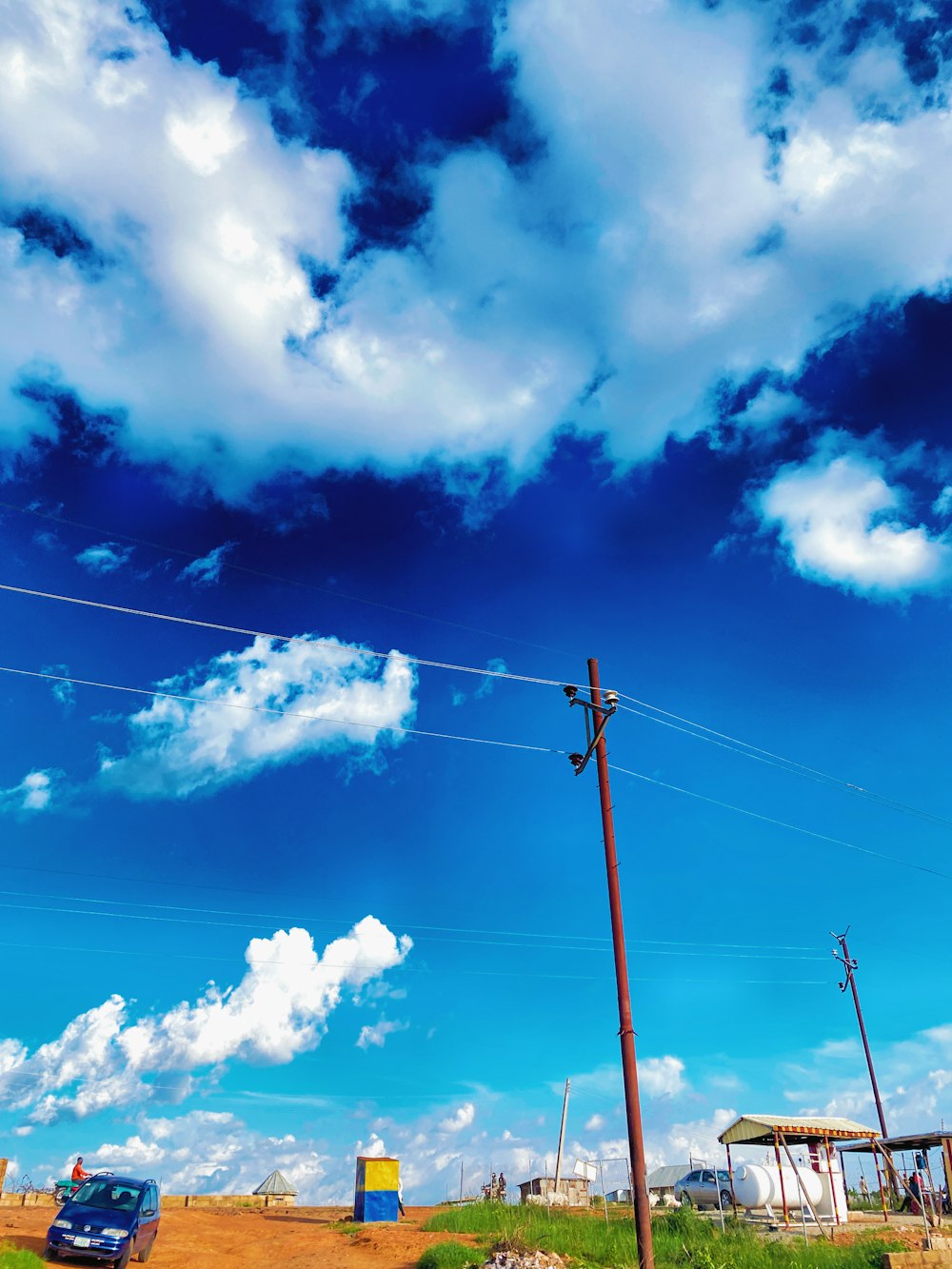 a car driving down a dirt road under a cloudy blue sky