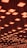 A ceiling installation featuring numerous square light fixtures, each emitting a warm, orange glow. The lights are arranged in a grid pattern and are suspended at varying heights, creating a visually dynamic effect.