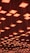 A ceiling installation featuring numerous square light fixtures, each emitting a warm, orange glow. The lights are arranged in a grid pattern and are suspended at varying heights, creating a visually dynamic effect.