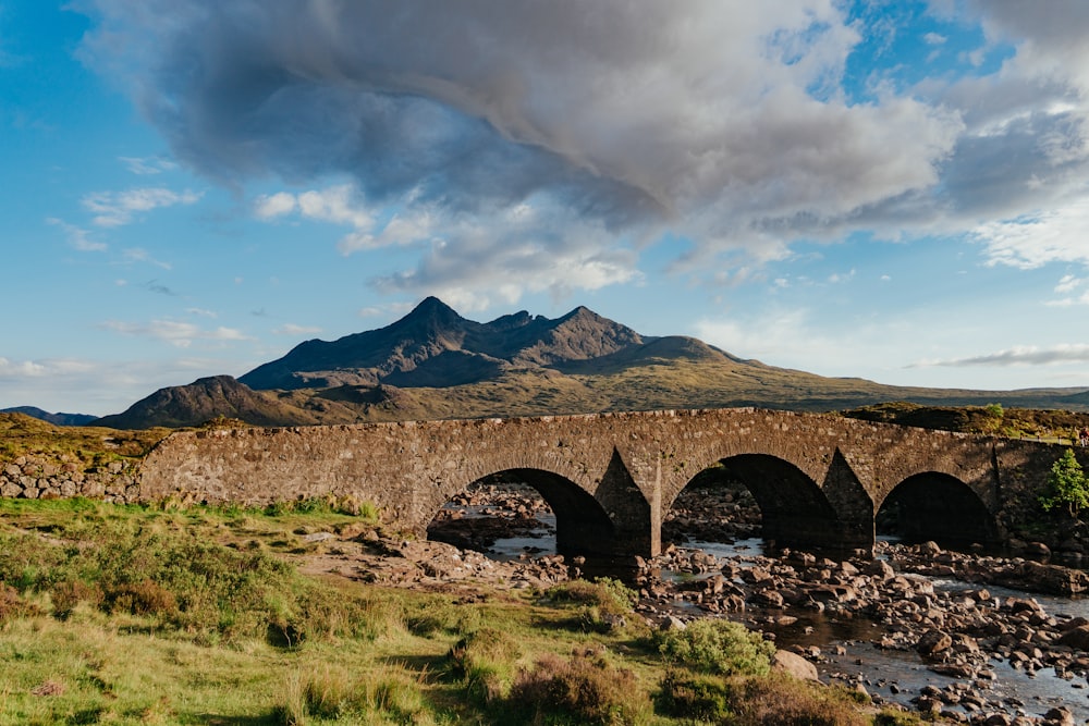 a stone bridge over a river with mountains in the background