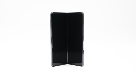 A modern foldable smartphone with a sleek design is open, showing its dual screen capabilities. The device appears to be in a vertical orientation against a plain, light background.