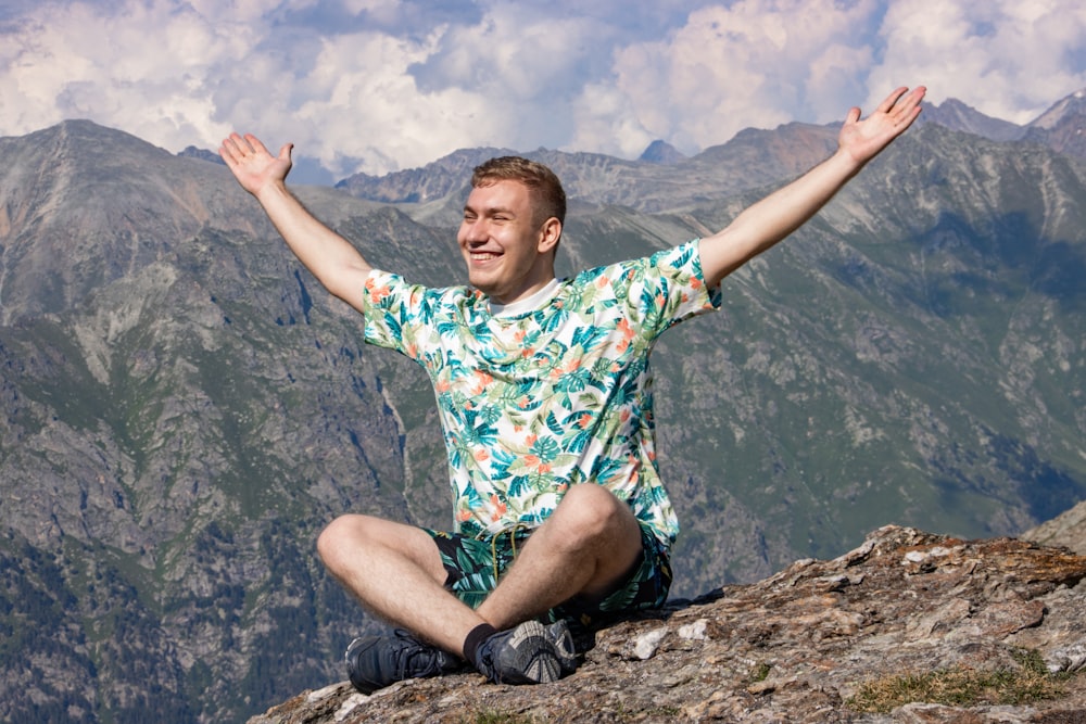 Un hombre sentado en la cima de una montaña con los brazos abiertos