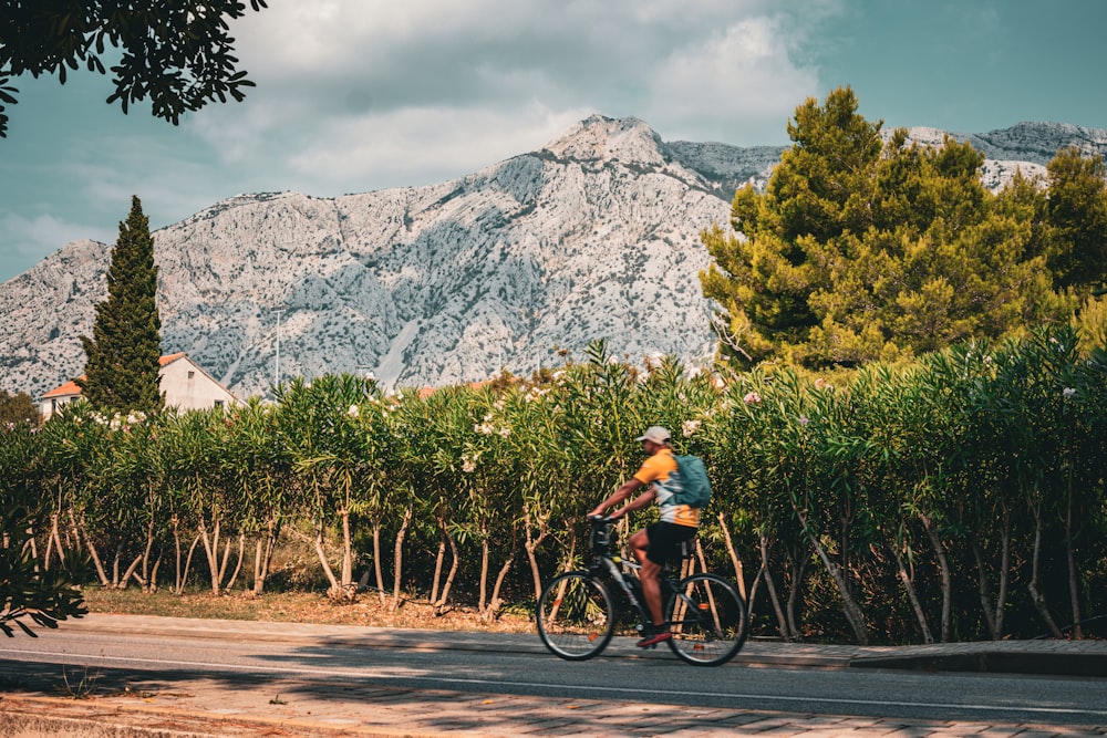 um homem andando de bicicleta por uma rua ao lado de uma floresta verde exuberante