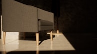 A modern gray sofa with light wooden legs sits in a room with minimalistic decor. Sunlight creates a dramatic pattern on the polished floor, highlighting the clean lines of the furniture. The background is dark, with a subtle texture on the walls, which enhances the contrast between the illuminated area and the shadows.