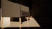 A modern gray sofa with light wooden legs sits in a room with minimalistic decor. Sunlight creates a dramatic pattern on the polished floor, highlighting the clean lines of the furniture. The background is dark, with a subtle texture on the walls, which enhances the contrast between the illuminated area and the shadows.