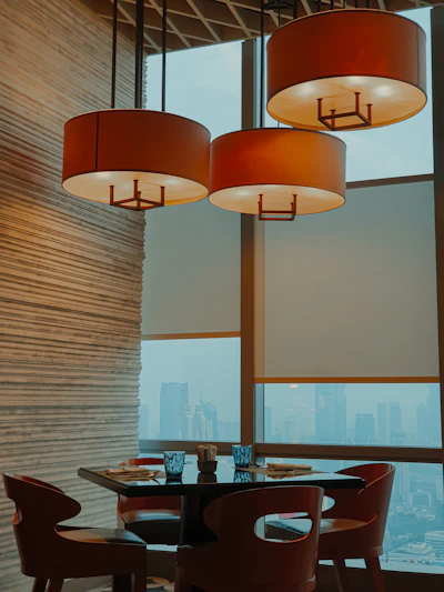 A sleek, handcrafted solid teak dining table set in a sunlit luxury apartment overlooking the Singapore skyline.