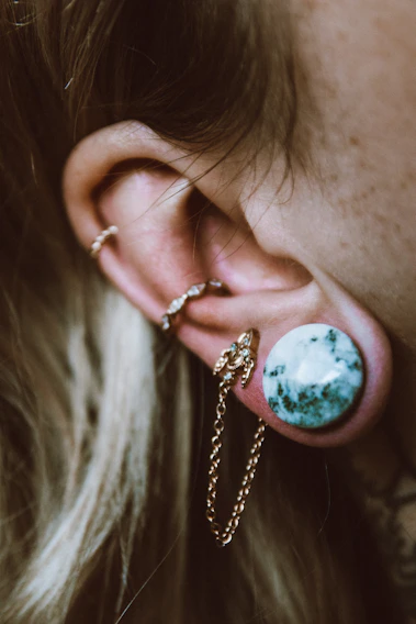 Close-up photo of elegant golden and green deep-tone piercings delicately arranged on a beige fabric background.