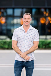 A warm portrait of a friendly real estate agent standing in front of a stylish modern home with soft natural light.