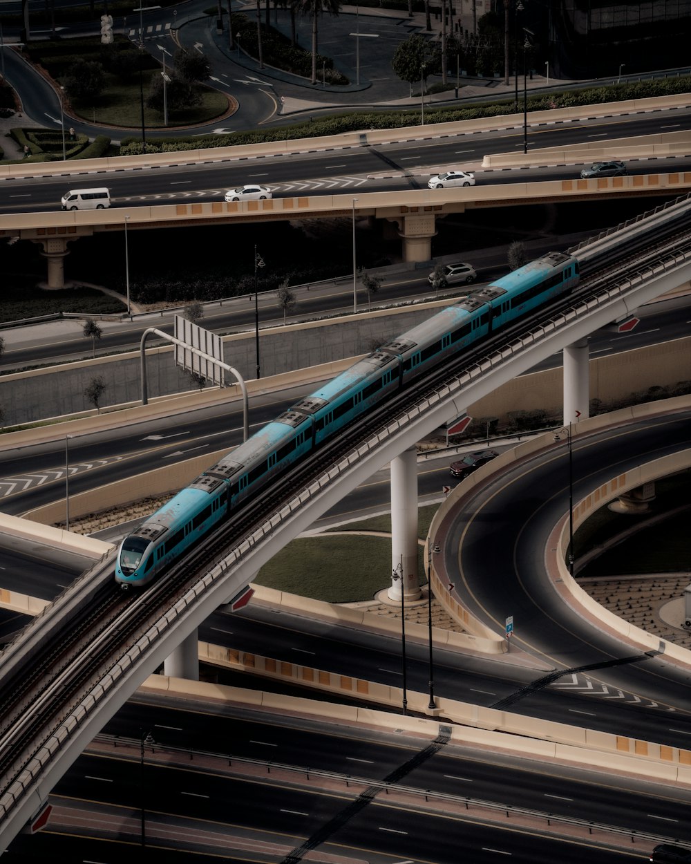 a blue train traveling over a bridge over a highway