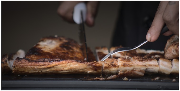Elegant close-up of a hand slicing thin jamón slices with a sharp knife at a sophisticated event.